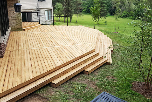 Custom wooden deck with stairs leading into open, green landscape.